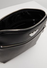 Borsa in pelle nera con hardware in argento, dotata di cerniere e una superficie testurizzata. L'interno include scomparti per l'organizzazione.