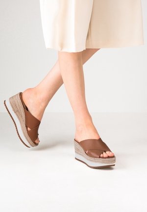 Brązowe sandały na koturnie z szerokim paskiem, posiadające naturalną podeszwę w stylu juty oraz teksturowany jasnoszary akcent na pięcie.