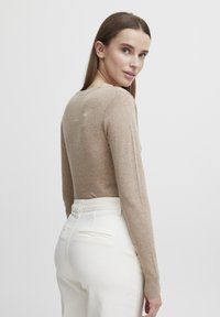 Un pull beige à manches longues avec un col rond, une coupe ajustée et une texture douce, associé à un pantalon blanc taille haute avec des poches arrière.