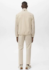 Lys beige jakke med høj krave, parret med matchende beige bukser. Designet med en afslappet pasform og elastiske manchetter.