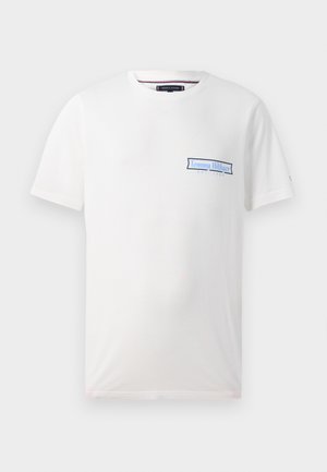 Vit bomull t-shirt med korta ärmar, med en blå logotyp på vänster bröstområde och design med rundad krage. Mjuk textur.