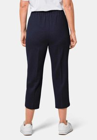 Marineblauwe cropped pants met een elastische tailleband, geribbeld textuur en zijnaaddetails, gecombineerd met witte sneakers.