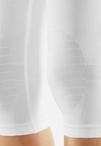 Witte compressieleggingen hebben een ribbelstructuur met horizontale lijnen en een elastische manchette aan de onderzijde. De stof lijkt glad en aansluitend.