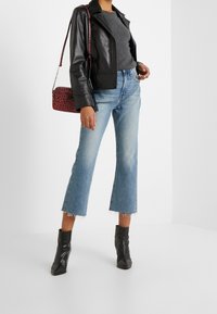 Chaqueta de cuero negra, blusa gris de manga corta, jeans cortos azul claro con dobladillo deshilachado y botas de tobillo negras con tacón; bolso de mano de leopardo rojo.