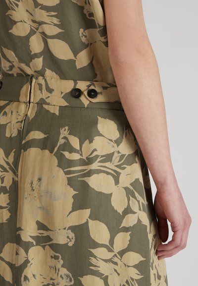 Robe à motifs floraux en vert olive avec des accents crème. Présente une taille ajustée avec deux boutons noirs et une texture de tissu visible.