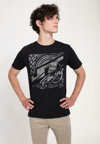 Svart t-shirt med en grafisk tryck av däckspår och racetext i silver. Tillverkad av mjukt tyg, med rund hals och korta ärmar.