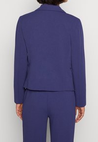 Fialový tailored blejzr se strukturovaným designem, dlouhými rukávy a klopovým límcem. Vyrobený z hladké látky; bez viditelných ozdob.