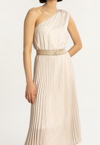 Asymetryczna sukienka na jedno ramię w jasnobeżowym kolorze, z teksturowaną górą i plisowanym dołem, dopasowana w talii brokatowym paskiem.