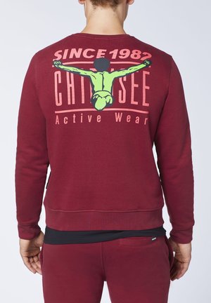 Maroon sweatshirt featuring a graphic on the back with the text "SINCE 1982" and a colorful illustration. Soft texture, crew neck design.