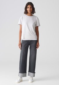 Grijze katoenen T-shirt met korte mouwen en een ronde halslijn, gecombineerd met wijde donkerdenim jeans met opgerolde manchetten en witte sneakers.