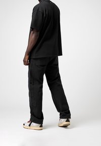 Zwarte katoenen oversized t-shirt en cargobroek, beide met een relaxte pasvorm; voorzien van zijzakken en textuurelementen; gecombineerd met sneakers.