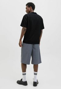 Chemise noire à manches courtes avec un motif en losanges texturé, associée à un short gris jusqu'aux genoux et des chaussures noires, complétée par des chaussettes blanches à rayures noires.