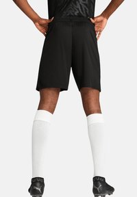 Schwarze sportliche Shorts aus leichtem Material, mit glatter Textur und lockerer Passform, kombiniert mit weißen knielangen Socken.