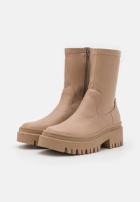 Botas de tobillo beige con punta redonda, cremallera lateral, textura de cuero suave y suela plataforma ancha y acanalada.