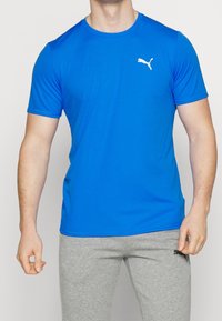 Modré sportovní tričko s krátkým rukávem vyrobené z hladké, lehké tkaniny. Obsahuje bílé logo Puma na levé části hrudi.