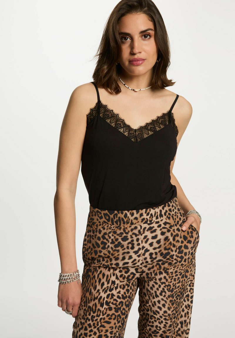 Top nero con pizzo, abbinato a pantaloni larghi con stampa leopardata. Presenta spalline sottili e tasche. Il materiale appare morbido e leggero.