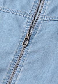 Close-up of a silver zipper on light blue denim fabric with visible stitching and the brand name "Street One" on the zipper pull.