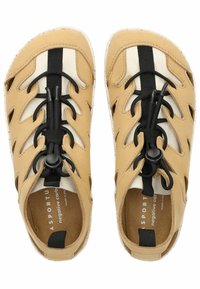 Světle hnědé sandály s vyřezávaným designem, černým elastickým šněrovacím systémem a texturovanou podrážkou. Interiér je vybaven světlým tkaninovým podšívkou.