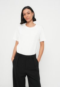 T-shirt en coton blanc avec un col rond et des manches courtes, associé à un pantalon noir taille haute avec poches latérales et une coupe décontractée.