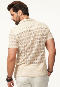 Strick-T-Shirt mit kurzen Ärmeln in Hellbeige, ausgestattet mit einem strukturierten Spitzenmuster, klassischem Kragen und offener Webstruktur.