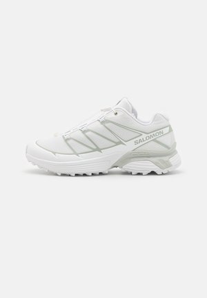Hvite sporty sko med teksturert mesh-overdel, reflekterende detaljer og en robust såle. Har elastiske lisser for sikker passform og stabilitet.