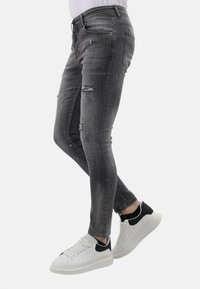 Skinny jeans in vervaagd zwart denim met scheuren, gecombineerd met witte sneakers met zwarte accenten. Gladde textuur, aansluitend ontwerp.