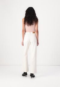 Wide-leg white jeans with a high waist, cotton fabric, back pockets, and a tan leather tag on the waistband. Paired with a pink ribbed tank top.