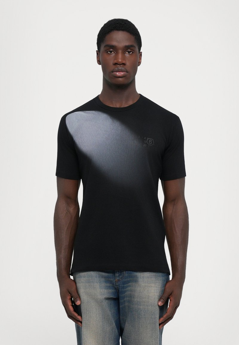 Svart t-shirt med gradientdesign och en liten grafisk tryck på bröstet. Tillverkad av mjukt tyg, med korta ärmar och rundad halsringning.