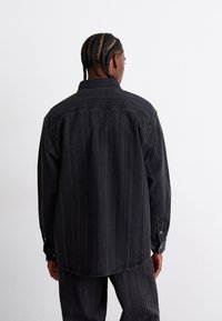 Chemise en denim noire à rayures avec manches longues, col au dos et détails de boutons sur les poignets. Tissu texturé avec un design à coupe ample.