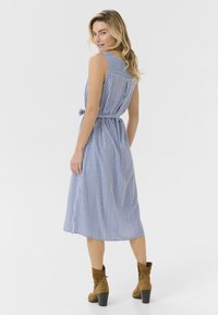 Vestido midi a rayas azul y blanco con cintura atada, diseño sin mangas y detalles en la parte posterior. Llevado con botas tipo botín marrón.