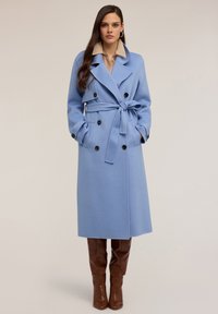 Długi niebieski płaszcz z mieszanki wełny, dwurzędowy z czarnymi guzikami, z paskiem w talii, szerokimi klapami i bocznymi kieszeniami. Połączony z brązowymi botkami do kolan.
