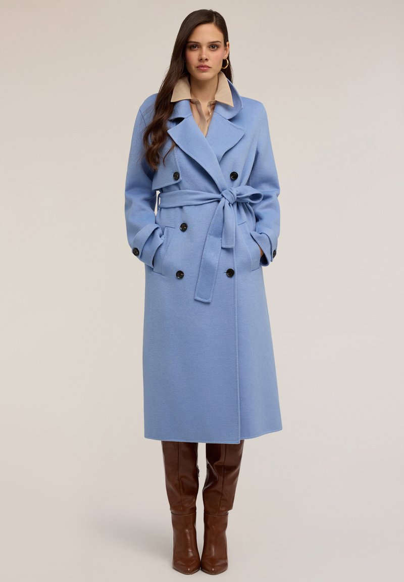Długi niebieski płaszcz z mieszanki wełny, dwurzędowy z czarnymi guzikami, z paskiem w talii, szerokimi klapami i bocznymi kieszeniami. Połączony z brązowymi botkami do kolan.