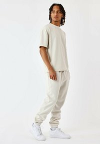 Camiseta corta de manga con textura suave en color beige claro, combinada con pantalones de chándal a juego con cordones. Completo con zapatillas blancas y un ajuste relajado.