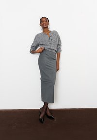 Hallituskrõmpsuga hall kardigan ümmarguse kaelusega, millele on lisatud sobiv hall penaskuus ja mustad terava ninaga kontsad. Siledad tekstuurid ja sale siluett.