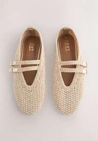 Paire de ballerines Mary Jane beige tissées avec double bride et boucles, étiquetées "Next Forever Comfort" à l'intérieur.