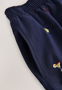 Pantalon en tissu texturé bleu marine avec taille élastique et détails brodés de verre à cocktail et tranche de citron près de la poche.
