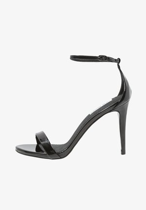 Sandalia de tacón alto de charol negro con tira al tobillo. Presenta una banda frontal ancha y un acabado suave y brillante. Tacón de aguja de 12 cm.