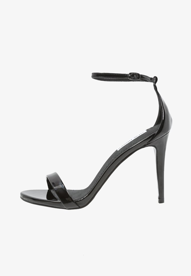 Sandale à talon haut en cuir verni noir avec une bride de cheville. Présente une large bande avant et une finition lisse et brillante. Talon stiletto de 12 cm.