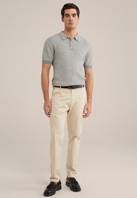 Polo shirt grigio con texture, maniche corte e righe verticali, abbinato a chinos beige chiaro e mocassini neri. Design semplice, bottoni al collo.