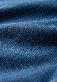 Džinsa audums dziļi zilos toņos ar gludu, strukturētu virsmu un smalkām diogonālām aušanas rakstām, rādot krokas un grumbas.