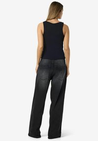 Top de tirantes azul marino hecho de tela acanalada, combinado con unos pantalones vaqueros de mezclilla negra de corte holgado, con detalles desgastados y bolsillos traseros clásicos.