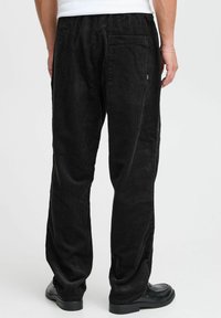 Pantalones de pana negra con diseño de pierna recta, cinturilla elástica y un bolsillo trasero. La textura es acanalada y suave.