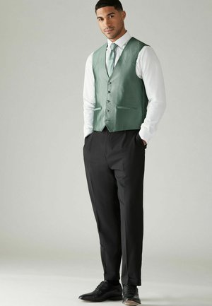 Green textured vest with six buttons, paired with white shirt and black dress pants. Black shoes. Simple, tailored design.