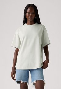 Lysegrøn oversized t-shirt lavet af blødt stof; korte ærmer og rund halsudskæring; bæres med slidte denimshorts. Enkel og minimalistisk design.