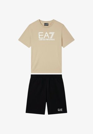 Maglietta beige a maniche corte con logo bianco "EA7 Emporio Armani" abbinata a pantaloncini neri con piccolo logo bianco EA7.