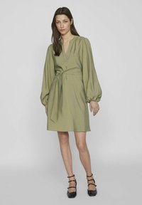 Olivgrön klänning med ballongärmar, V-ringning och knytmidja. Sl�ät tyg med en lätt lyster, matchad med svarta strappy heels.