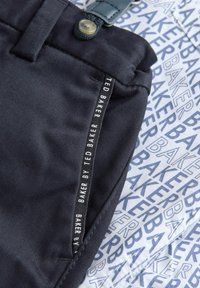 Granatowy materiał o gładkiej teksturze, z paskiem w talii z guzikiem oraz metką z napisem "BAKER BY TED BAKER" na tle niebieskiego wzoru.