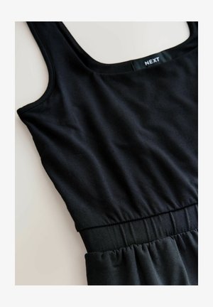 Čierne bezrukávové šaty so zrolovaným pásom a viditeľnou nálepkou "NEXT" na vnútornej zadnej časti výstrihu, položene na svetlom povrchu.