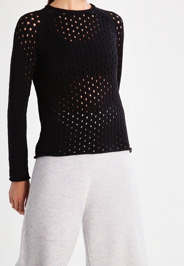 Svart stickad långärmad topp med ett nätmönster och stora hål. Rund halsringning och figurnära midja. Styklad med ljusgrå vida byxor.