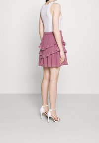 Jupe à volants rose avec des bords froncés et des détails texturés, associée à des talons hauts blancs à brides. Modèle portant un débardeur blanc ajusté.